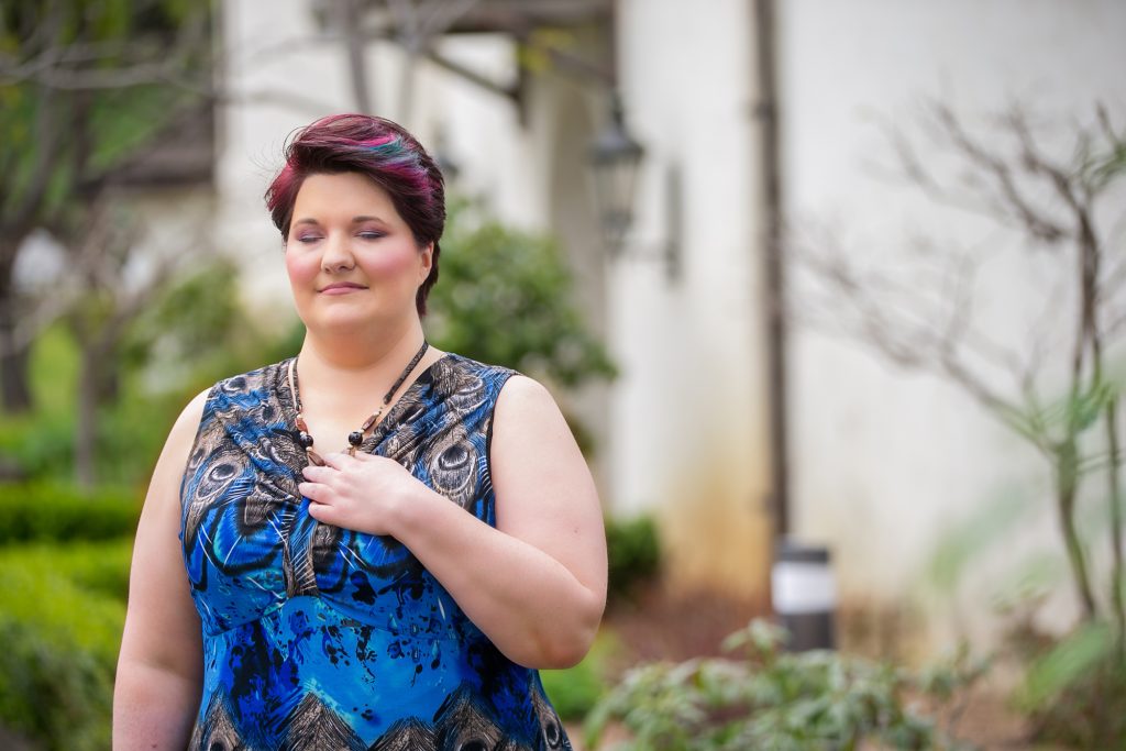 Woman smiling peacefully in a garden setting wearing blue dress