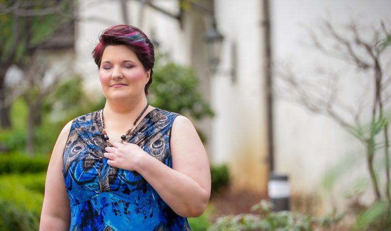 Woman smiling peacefully in a garden setting wearing blue dress