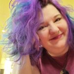 Smiling person with vibrant purple and blue hair indoors