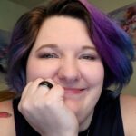 Smiling individual with colorful short hair looking content