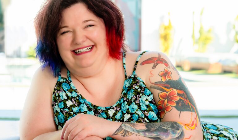 Smiling woman with colorful tattoos and floral dress indoors
