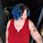 Person with blue hair and tattoos in a red sleeveless top