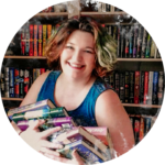 Person smiling while holding a stack of colorful books