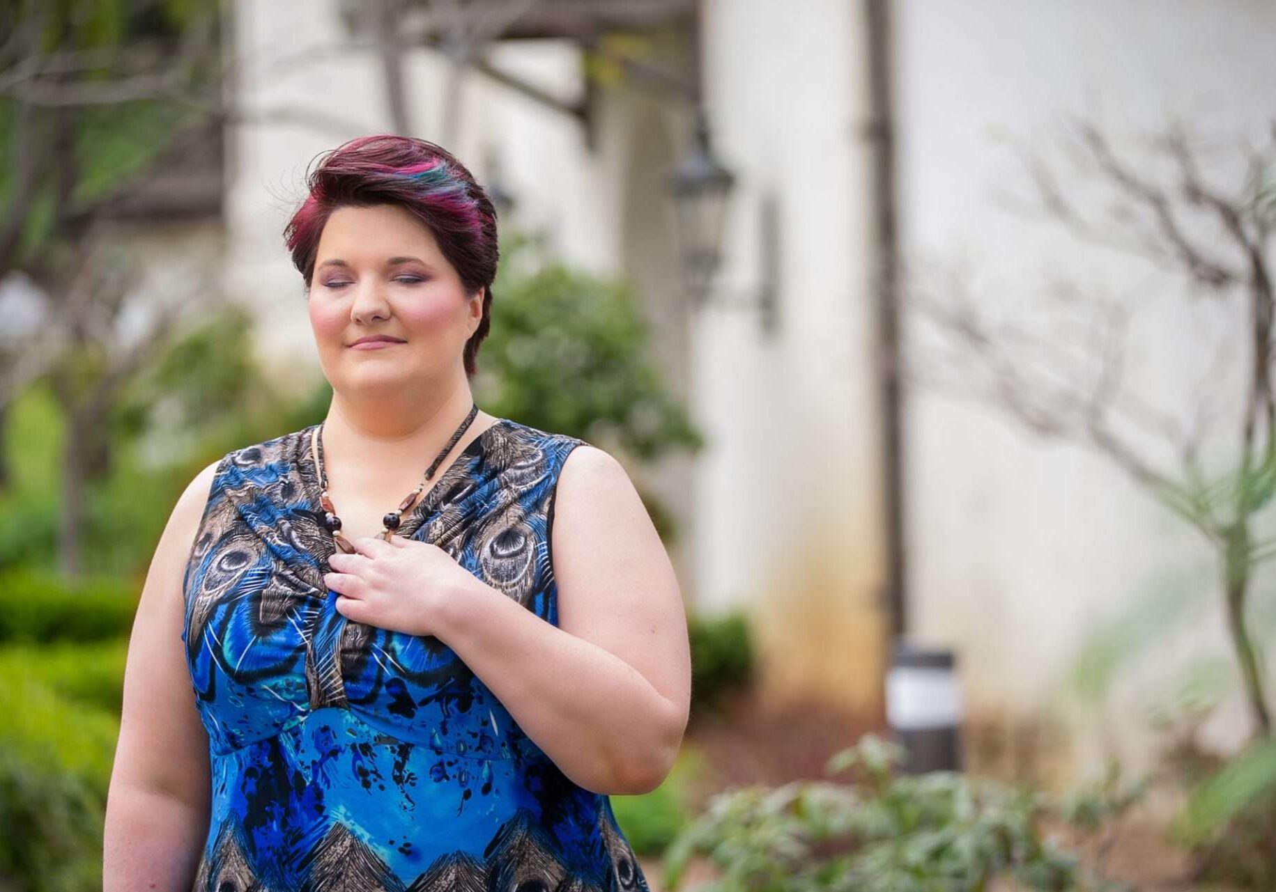 Woman smiling peacefully in a garden setting wearing blue dress