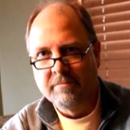 Middle-aged man wearing glasses near a window with blinds